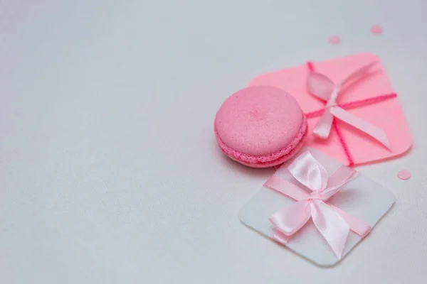 Sweet pink macaroons with gifts on a white background. Flat lay.