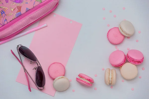 White background with pink and white macaroons, with pink glasses and a cosmetic bag, with pink decor.