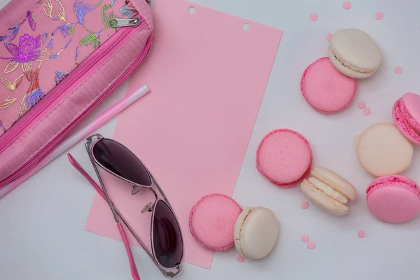 White background with pink and white macaroons, with pink glasses and pencil case, with pink decor.