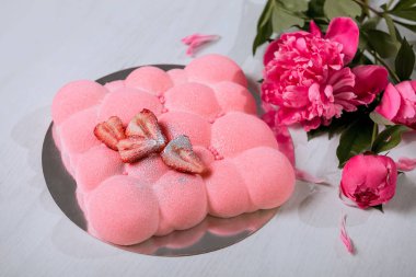 Çilekli kremalı pasta masanın üzerinde duruyor. Bir buket pembe şakayık..