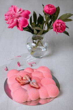 Çilekli kremalı pasta masanın üzerinde duruyor. Bir buket pembe şakayık..