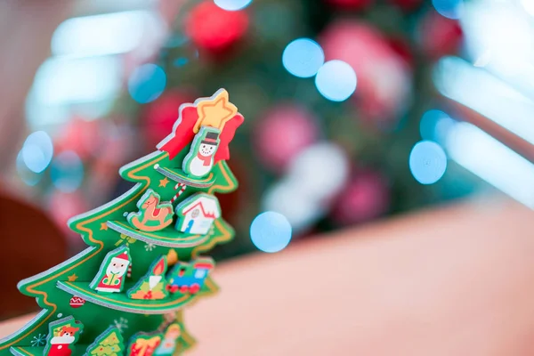 Christmas tree paper craft decoration on the wood table with blur big Christmas tree behide.