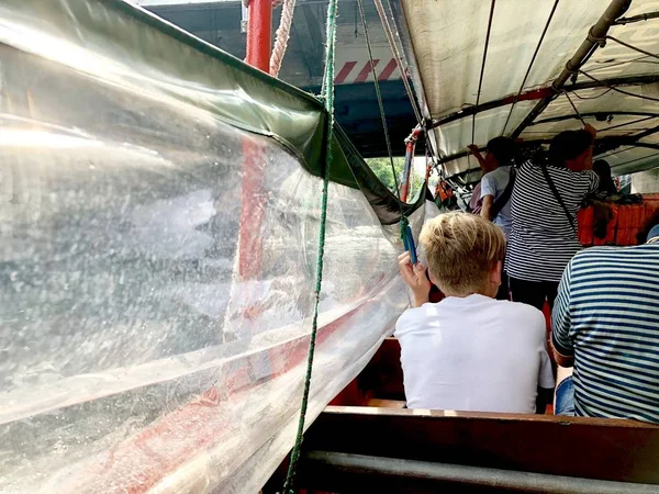 blonde boy siting in the canal boat, he hold the robe for pull up transperence canvas to protect the splash water come inside., Thailand San Sarb canal transportation.