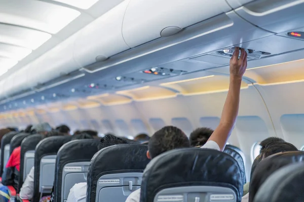 Asian couple people cabin crew, hand up to adjust console panel; the air condition, light / lamp above the low cost airline seat.