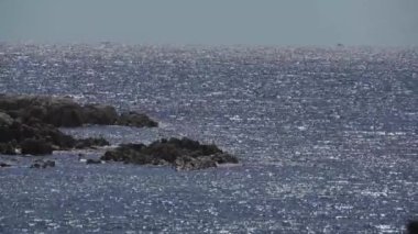 Ortasında siyah-kahverengi kaya ile denizde parlak güneş ışığı reflenyon.