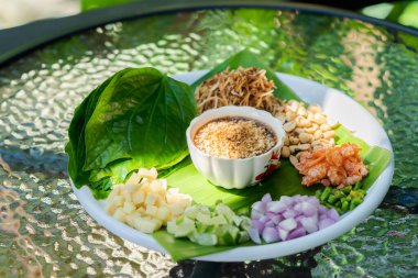 Miang kham, Tayland ve Laos 'tan geleneksel bir Güneydoğu Asya aperatifi. Açık hava masasındaki güneş ışığıyla birlikte beyaz tabağın üzerinde..
