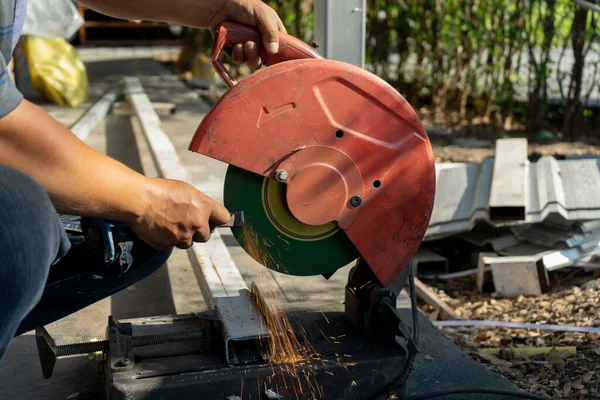 Asian Construction worker is sharpening chisel by big blade machine at outdoor field with tree in the row background.