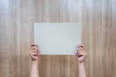 Asyalı kişi ahşap arka plandaki boş a4 kağıdını tutuyor ve kaldırıyor..