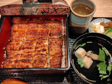 Klasik bir Japon setinde çorba, turşu ve sıcak çay eşliğinde ızgara yılan balığıyla servis edilen laktüel bir kutu yemek. Sunumda denge ve lezzete dikkat ederek geleneksel akşam yemeklerine vurgu yapılıyor.