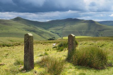 Güneşli dağları ve tepesinde kara bulutlar olan taş kapı direklerini, İngiltere 'nin Peak District bölgesini gör.