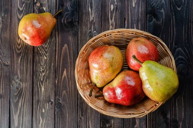 Koyu ahşap rustik arka plan üzerinde bir sepet içinde parlak kırmızı-sarı armut. Sonbaharda hasat meyve.