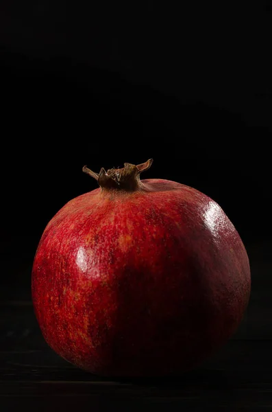 one ripe pomegranate on a black wooden background