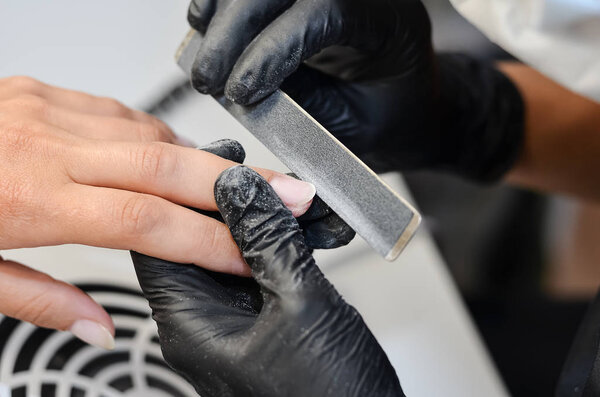 The master does hardware manicure in the beauty salon. Removal of the gel varnish with a milling cutter, removing the pterygium and cuticle with a remover, applying gel shellac varnish with a design.