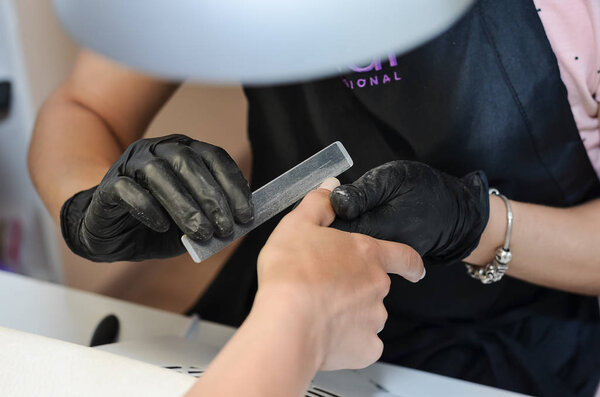 The master does hardware manicure in the beauty salon. Removal of the gel varnish with a milling cutter, removing the pterygium and cuticle with a remover, applying gel shellac varnish with a design.