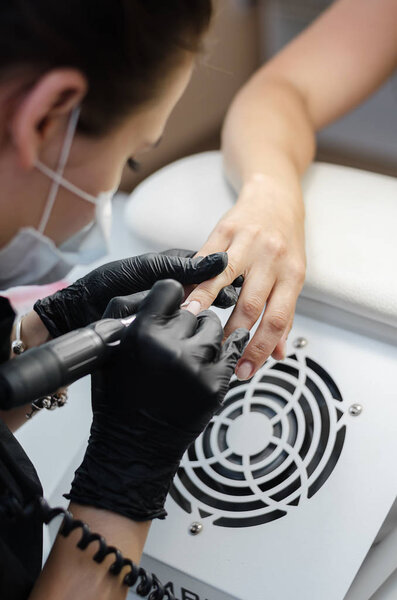 The master does hardware manicure in the beauty salon. Removal of the gel varnish with a milling cutter, removing the pterygium and cuticle with a remover, applying gel shellac varnish with a design.