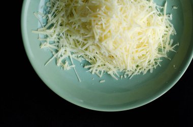 Karanlık bir arka plan üzerinde bir tabakta rendelenmiş parmesan peyniri