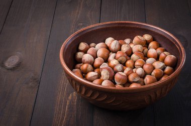 Bir karanlık, rustik, ahşap arka planda bir kil kase fındık.