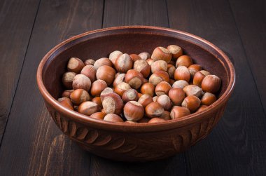 Bir karanlık, rustik, ahşap arka planda bir kil kase fındık.