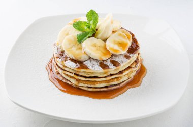 Muz dilimleri ve karamel sos, nane ile süslenmiş krep yığını.