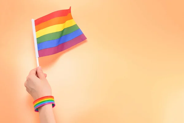 Bandeira LGBT na mão da mulher no fundo laranja. Espaço de cópia . — Fotografia de Stock