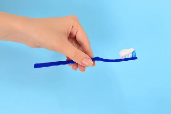 Woman holds toothbrush with toothpaste in her hand on a blue bac — Stock Photo, Image