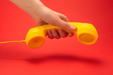 Kadın elinin kırmızı arka planında sarı bir cep telefonu. Boşluğu kopyala.