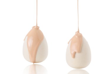 Beyaz arka planda izole edilmiş yeni beyaz süngerin üzerine dökülen sıvı bej makyaj vakfı