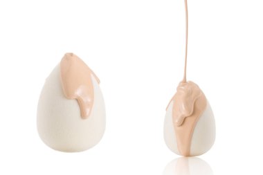 Beyaz arka planda izole edilmiş yeni beyaz süngerin üzerine dökülen sıvı bej makyaj vakfı