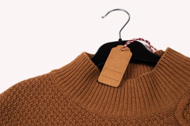 Örgü süveter etiketli siyah bir askıda asılı. Beyazda izole edilmiş.