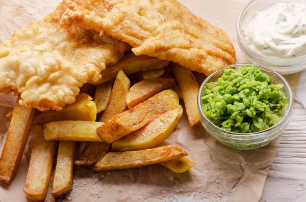 Traditional British street food fish and chips with mushy peas and tartar sauce on parchment paper