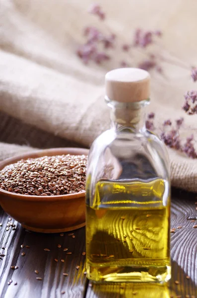 Flax oil and raw seeds in wooden bowl on kitchen table closeup