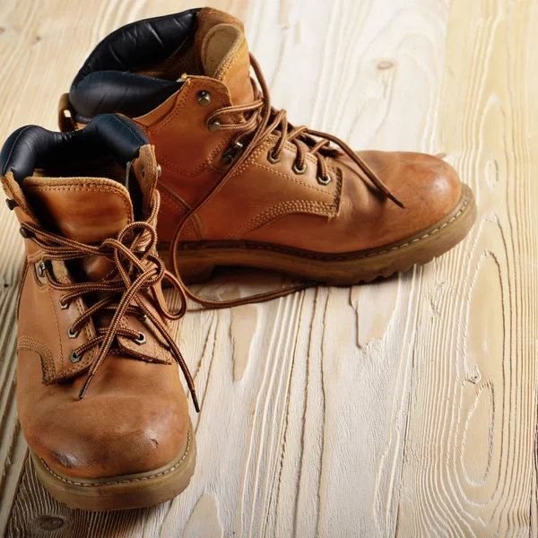 Yellow leather used work boots on wooden background closeup. Pla