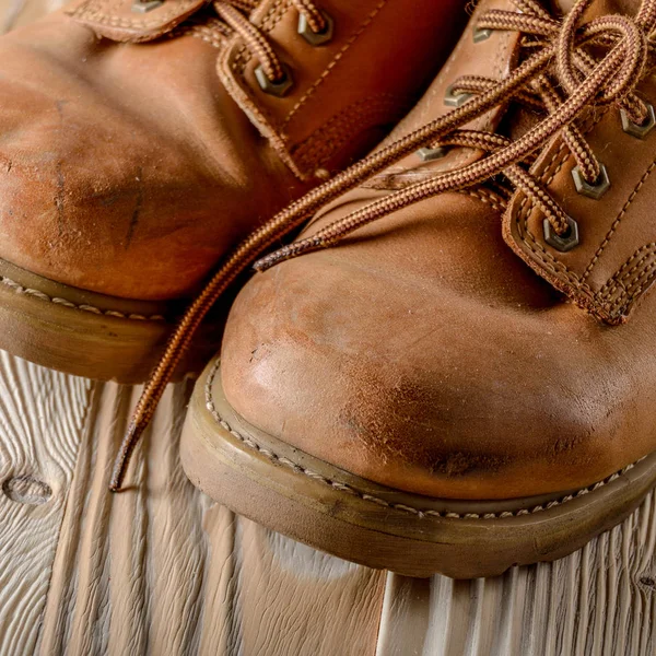 Yellow leather used work boots on wooden background closeup. Pla