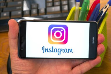 Piatra Neamt, Romanya - 30 Temmuz 2018: El üstünde belgili tanımlık perde, office arka plan Instagram logolu cep telefonu tutan.