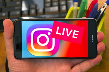 Piatra Neamt, Romanya - 30 Temmuz 2018: El üstünde belgili tanımlık perde, office arka plan Instagram Live logolu cep telefonu tutan.