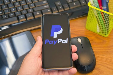 Piatra Neamt, Romanya - 30 Temmuz 2018: El Samsung S8 + Paypal ile tutan üstünde belgili tanımlık perde, office arka plan.