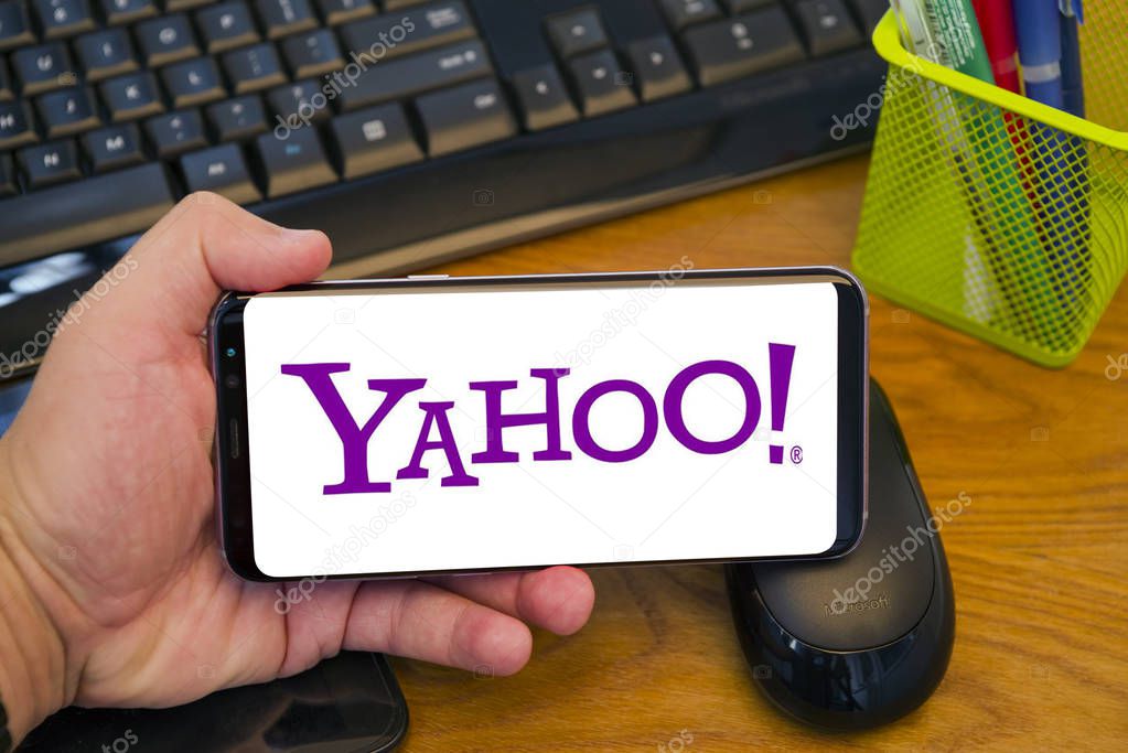 PIATRA NEAMT, ROMANIA - JULY 30, 2018: Hand holds a Samsung S8+ with Yahoo company logo on the screen, office background.