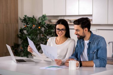Analitik planlama. Kağıtları tutarak ve kendi iş üzerinde çalışırken mutfakta oturmuş neşeli yougn çift