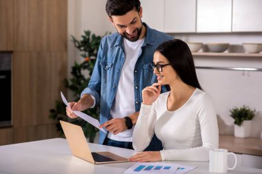 Bir göz atın. Genç kocasının yakın ayakta iken dizüstü bilgisayarda çalışan neşeli kadın