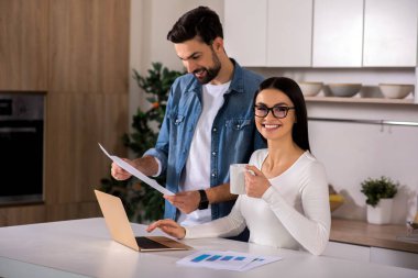 Pozitifliği paylaşmak. Mutfak ve kocası yakın duran otururken onu laptop kullanan neşeli güzel kadın