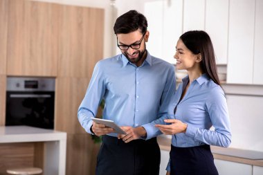 Duyguları paylaşmak. Tablet kullanma ve mutfakta çay içme neşeli iş arkadaşları