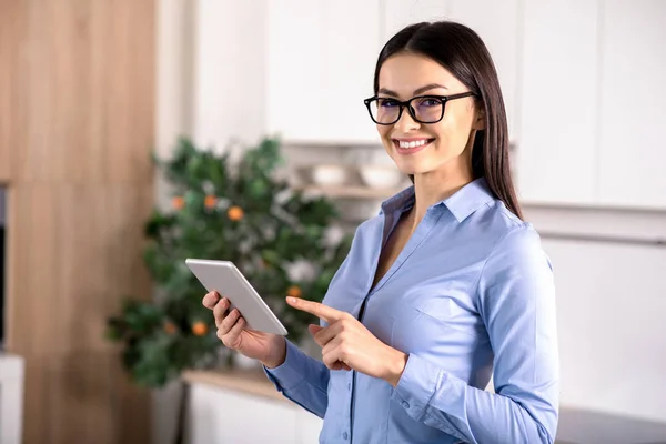 Business attitude. Positive nice woman using her tablet while standing in the kitchen