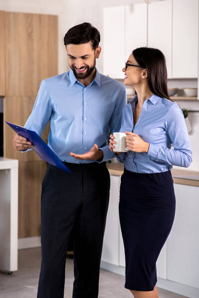 Positive relations. Cheerful yougn business colleagues standing in the kitchen while having a rest after work
