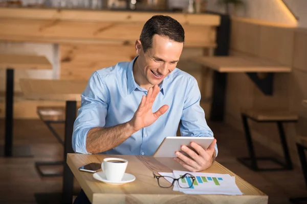 Усміхнений Бізнесмен Сидить Кафе Маючи Відеочат Допомогою Цифрового Планшета Махаючи — стокове фото