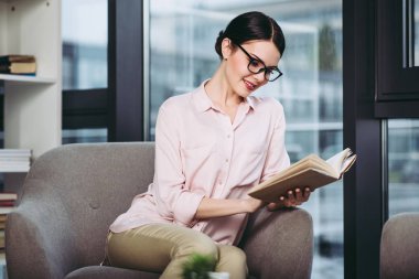 kitap okuma ve koltukta oturan gülümseyen iş kadını