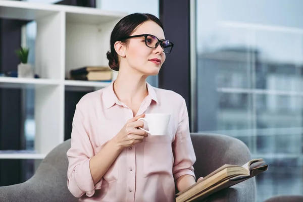 Pensativa Mujer Negocios Leyendo Libro Sosteniendo Taza Café Mientras Está —  Fotos de Stock