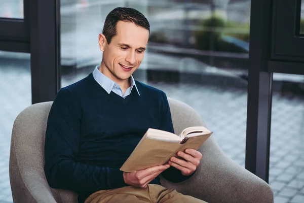 Souriant Caucasien Homme Lisant Livre Tout Étant Assis Sur Fauteuil — Photo