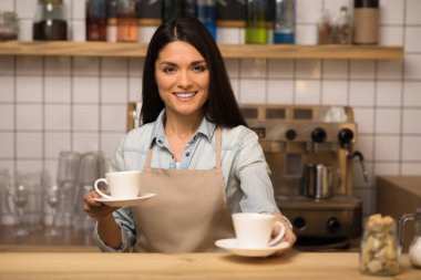 İki bardak kahve tutarak ve kameraya bakarak neşeli barista
