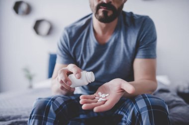 Beyaz adam yatakta otururken yandan konteyner hapları dökülmesini görüntü kırpılmış