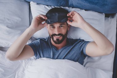Yatakta yatan ve kameraya bakarak uyku maskeli yakışıklı adam portresi